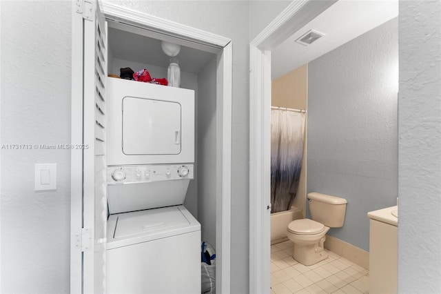 laundry area with stacked washer / drying machine, visible vents, a textured wall, and tile patterned floors