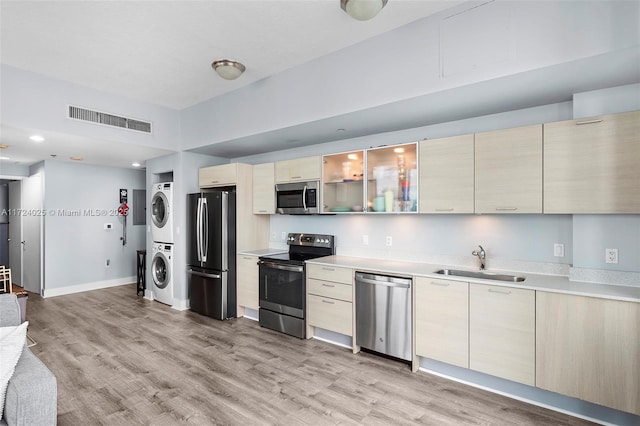 kitchen with sink, light hardwood / wood-style flooring, stacked washer and clothes dryer, and appliances with stainless steel finishes