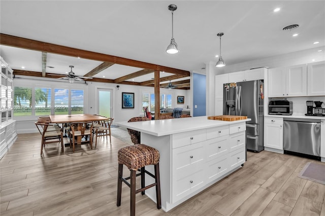 kitchen featuring stainless steel appliances, white cabinetry, a center island, and beam ceiling