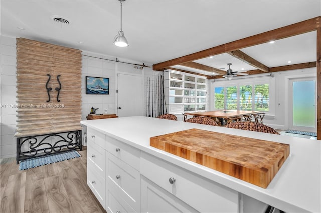 kitchen with pendant lighting, light hardwood / wood-style flooring, ceiling fan, white cabinetry, and beamed ceiling