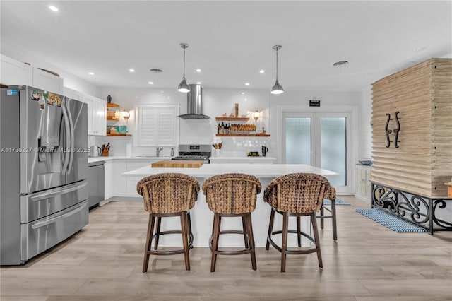 kitchen featuring wall chimney exhaust hood, stainless steel appliances, a center island, and white cabinets