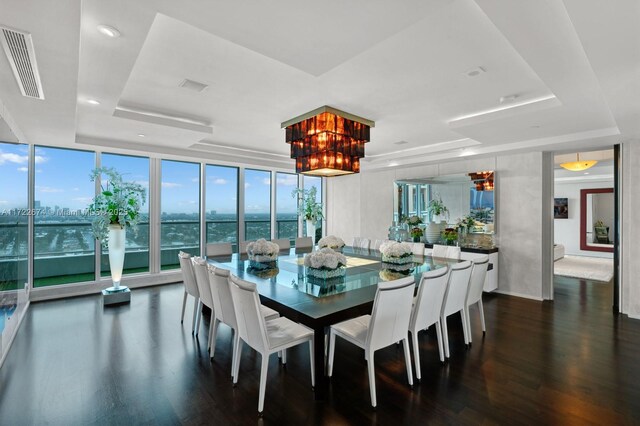 dining room with dark wood-type flooring, a raised ceiling, a wall of windows, and a water view