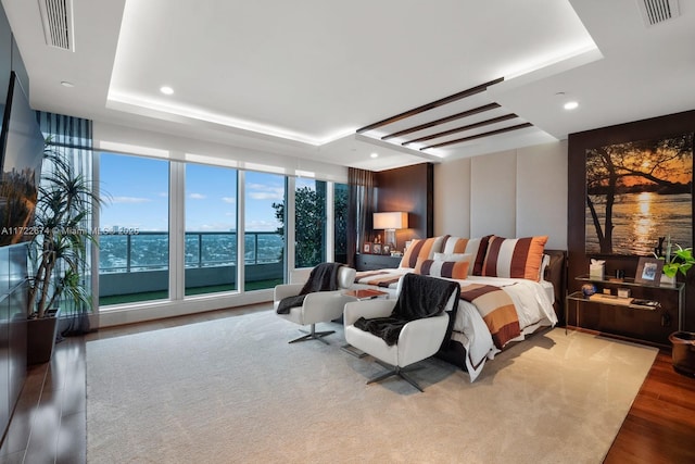 bedroom with expansive windows, a tray ceiling, and light wood-type flooring