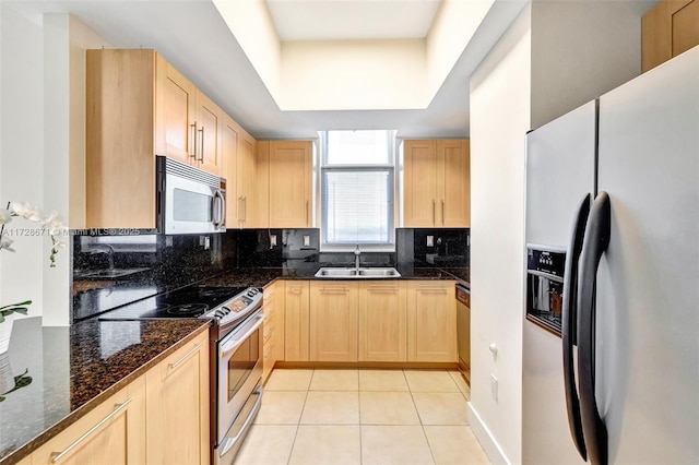 kitchen featuring sink, appliances with stainless steel finishes, light tile patterned flooring, light brown cabinetry, and dark stone counters