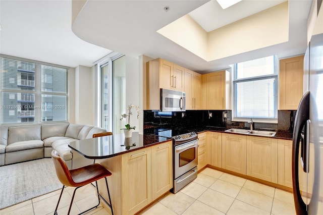 kitchen with appliances with stainless steel finishes, sink, light brown cabinetry, and kitchen peninsula