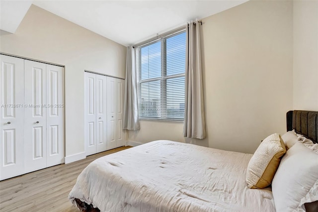 bedroom with multiple closets, vaulted ceiling, and light hardwood / wood-style floors