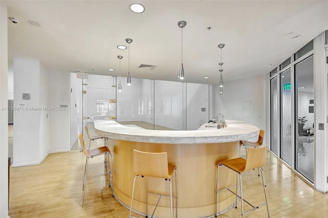 kitchen with hanging light fixtures, an island with sink, a breakfast bar, and light hardwood / wood-style flooring