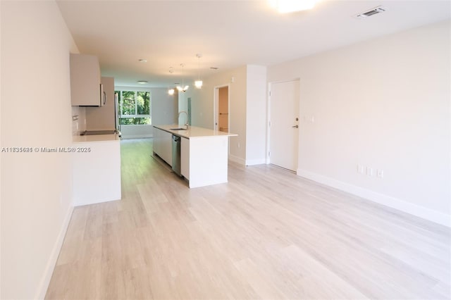 kitchen featuring pendant lighting, an island with sink, sink, stainless steel dishwasher, and light hardwood / wood-style flooring