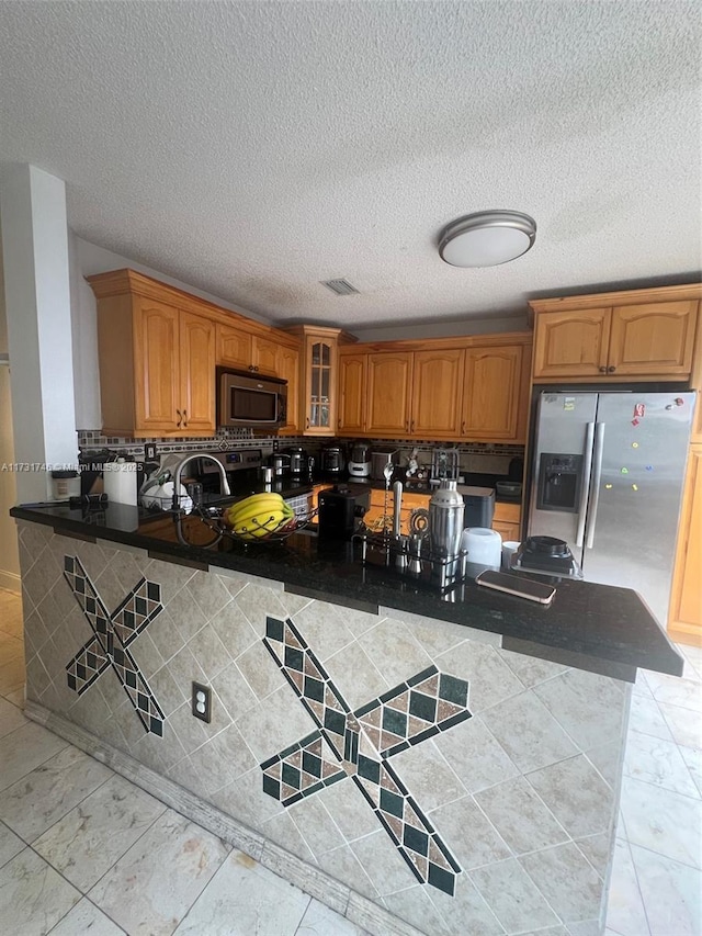 kitchen with appliances with stainless steel finishes, kitchen peninsula, sink, and a textured ceiling