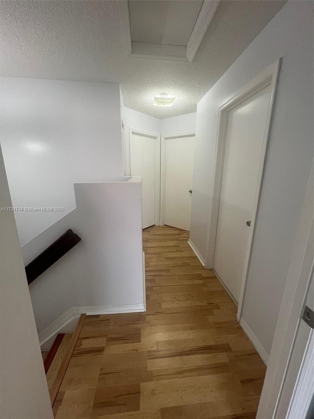 hall with a textured ceiling and light wood-type flooring