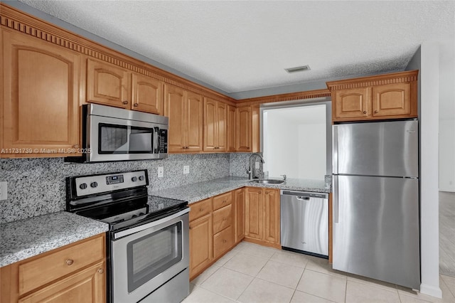 kitchen with sink, light stone counters, a textured ceiling, light tile patterned floors, and appliances with stainless steel finishes