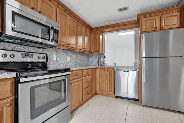 kitchen featuring light tile patterned flooring, sink, a textured ceiling, appliances with stainless steel finishes, and decorative backsplash