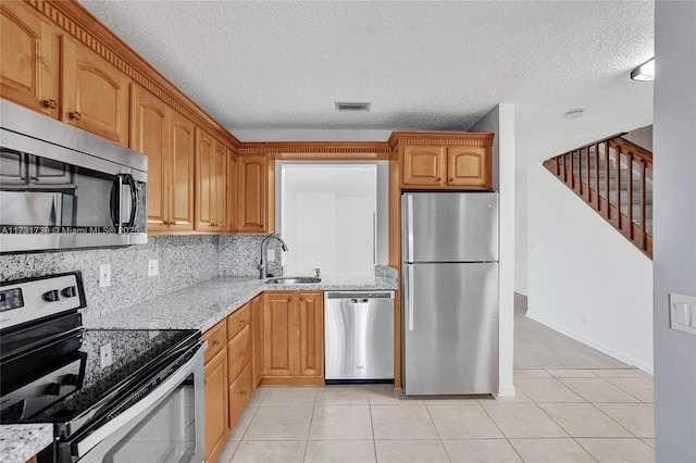 kitchen with appliances with stainless steel finishes, light stone countertops, sink, and light tile patterned floors