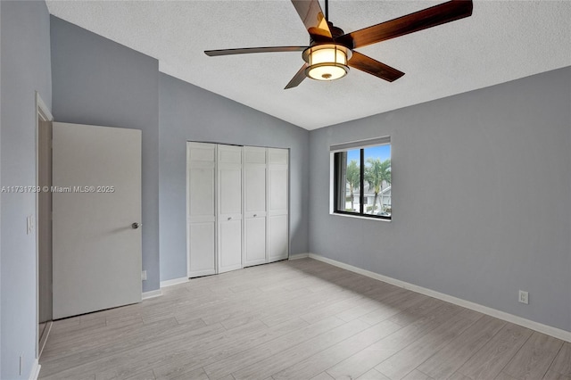 unfurnished bedroom with ceiling fan, lofted ceiling, a closet, and light wood-type flooring