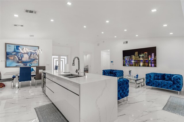 kitchen featuring lofted ceiling, sink, light stone counters, white cabinetry, and a center island with sink