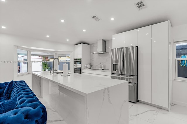 kitchen with wall chimney exhaust hood, stainless steel appliances, a kitchen island with sink, and white cabinets