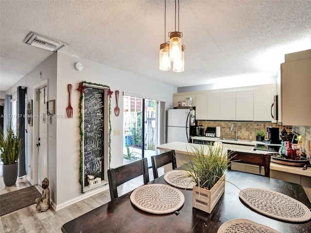 kitchen featuring sink, white cabinetry, white fridge, pendant lighting, and decorative backsplash