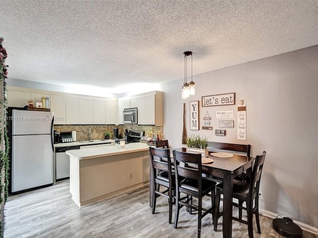 dining room with sink, a textured ceiling, and light hardwood / wood-style floors