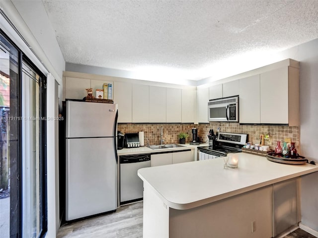 kitchen featuring stainless steel appliances, sink, a textured ceiling, and kitchen peninsula