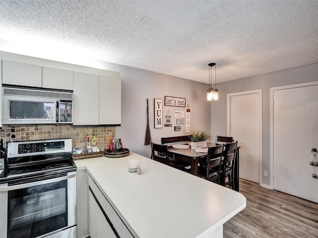 kitchen with appliances with stainless steel finishes, white cabinetry, backsplash, decorative light fixtures, and light wood-type flooring