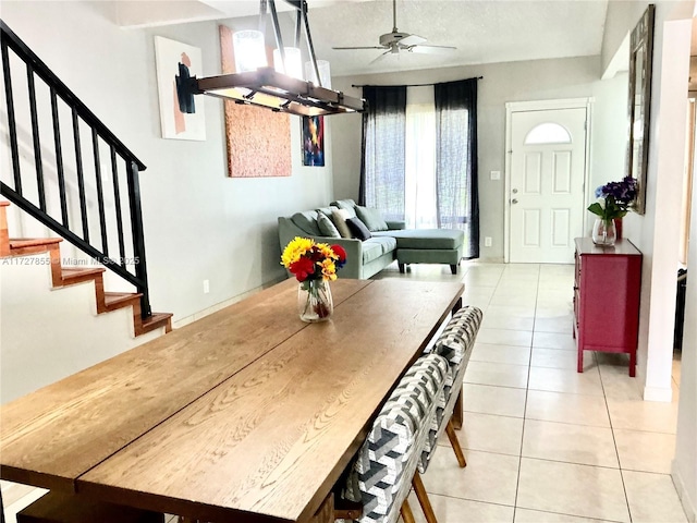 dining space featuring ceiling fan with notable chandelier, light tile patterned flooring, and stairs