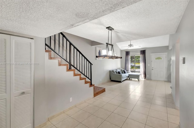 entryway featuring a ceiling fan, a textured ceiling, light tile patterned flooring, baseboards, and stairs