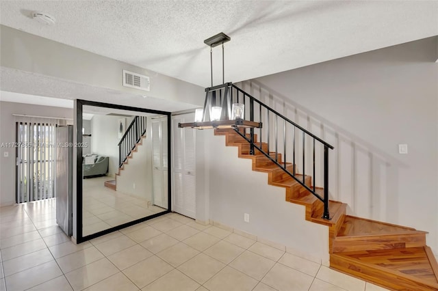 stairway featuring tile patterned floors, visible vents, and a textured ceiling