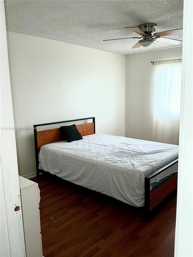 bedroom featuring dark wood-type flooring, ceiling fan, and a textured ceiling