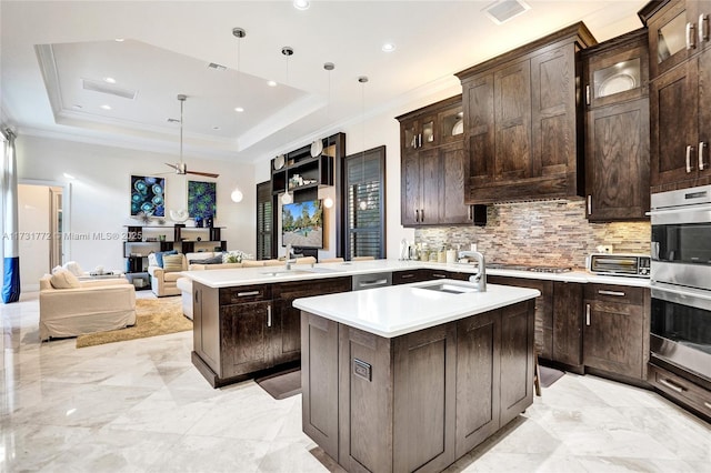 kitchen featuring pendant lighting, appliances with stainless steel finishes, a kitchen island with sink, dark brown cabinets, and a tray ceiling