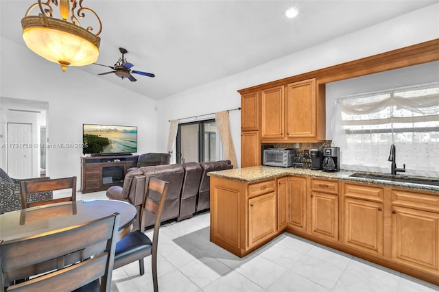 kitchen featuring sink, tasteful backsplash, vaulted ceiling, kitchen peninsula, and light stone countertops