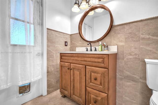 bathroom with tile walls, an inviting chandelier, vanity, tile patterned floors, and toilet