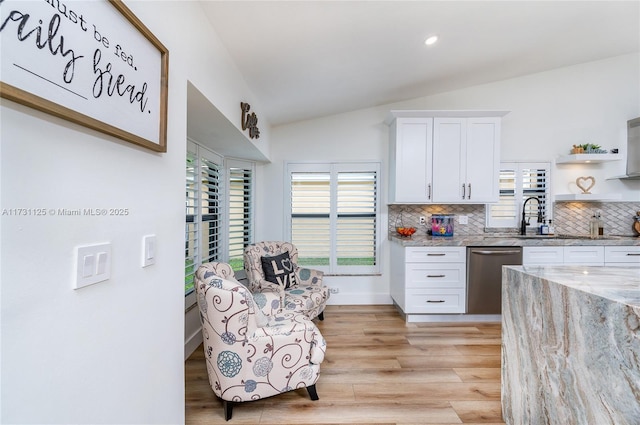 kitchen featuring tasteful backsplash, dishwasher, lofted ceiling, white cabinets, and light stone countertops