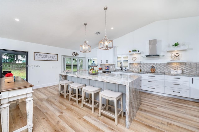 kitchen with wall chimney range hood, open shelves, white cabinetry, and lofted ceiling