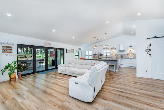 living room featuring a wealth of natural light, vaulted ceiling, a barn door, and light wood-type flooring