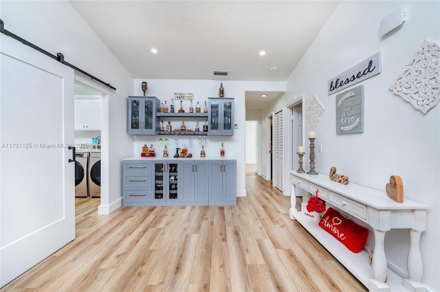 bar featuring washing machine and clothes dryer, a barn door, light hardwood / wood-style flooring, and gray cabinetry