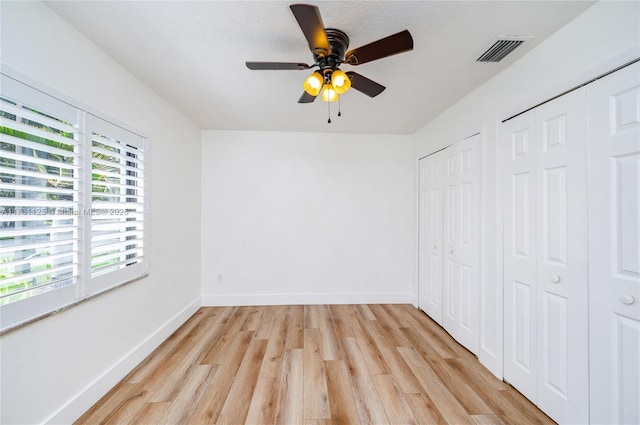 unfurnished bedroom featuring ceiling fan, light hardwood / wood-style flooring, and two closets