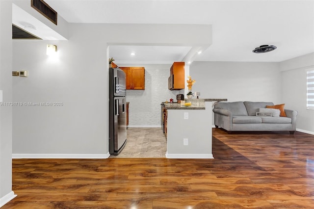 kitchen with stone counters, stainless steel fridge with ice dispenser, a breakfast bar area, dark hardwood / wood-style flooring, and kitchen peninsula