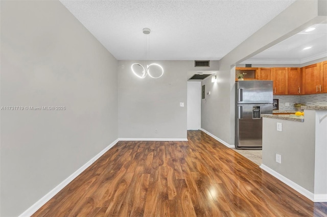 kitchen with pendant lighting, tasteful backsplash, wood-type flooring, stainless steel fridge with ice dispenser, and a textured ceiling