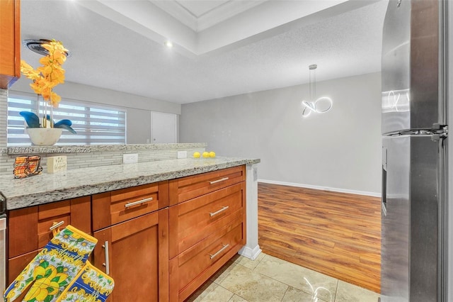 kitchen featuring light tile patterned floors, stainless steel fridge, hanging light fixtures, light stone counters, and a textured ceiling