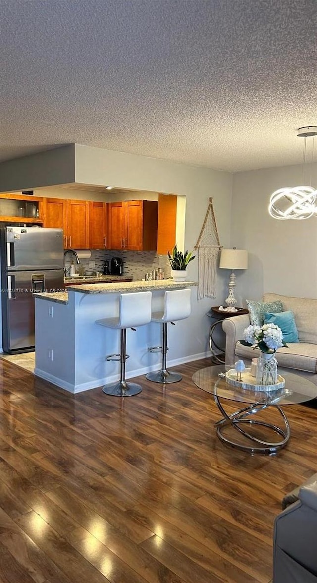 kitchen featuring dark wood-type flooring, stainless steel fridge, a kitchen breakfast bar, tasteful backsplash, and kitchen peninsula