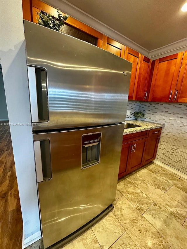 kitchen with crown molding, stainless steel fridge, light stone countertops, and decorative backsplash