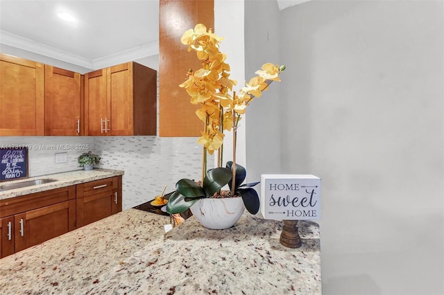 kitchen featuring light stone counters, sink, decorative backsplash, and ornamental molding