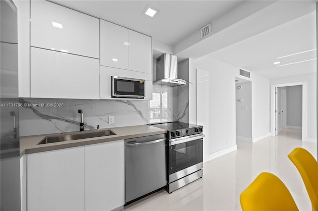 kitchen featuring tasteful backsplash, white cabinetry, sink, stainless steel appliances, and wall chimney exhaust hood