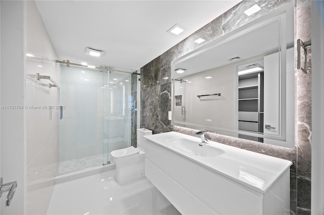 bathroom with toilet, tile walls, vanity, and a shower with shower door