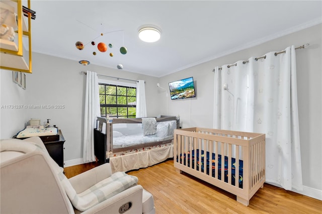 bedroom featuring crown molding, wood-type flooring, and a crib