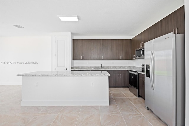 kitchen featuring light tile patterned floors, appliances with stainless steel finishes, dark brown cabinets, light stone counters, and a kitchen island