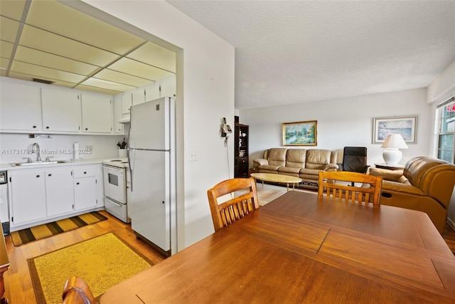 kitchen with sink, white cabinetry, a textured ceiling, white appliances, and light hardwood / wood-style floors