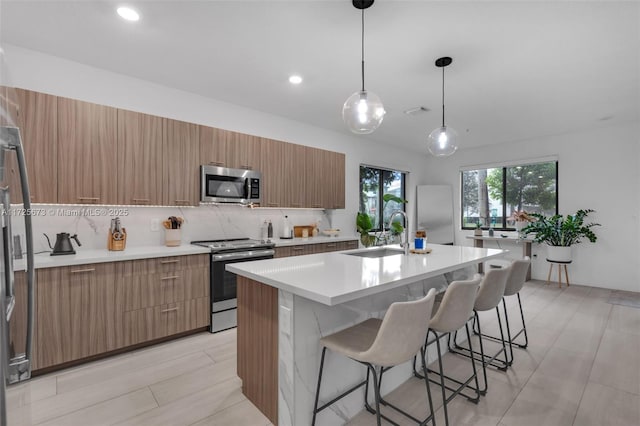 kitchen featuring pendant lighting, sink, appliances with stainless steel finishes, a center island with sink, and decorative backsplash