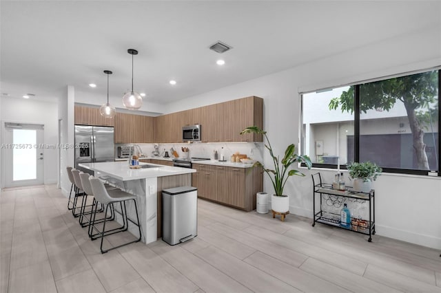 kitchen featuring a kitchen bar, a center island with sink, appliances with stainless steel finishes, pendant lighting, and decorative backsplash