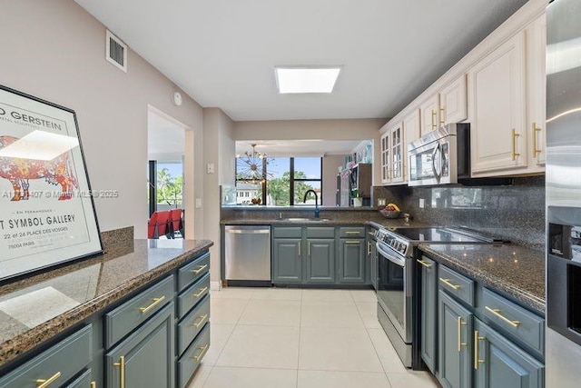 kitchen featuring light tile patterned floors, appliances with stainless steel finishes, white cabinetry, decorative backsplash, and dark stone counters